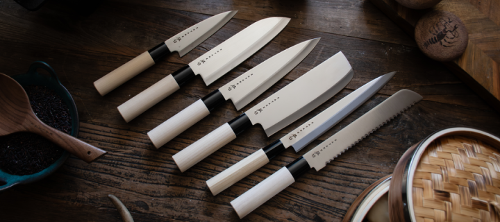 A collection of different types of Japanese knives laid out on a wooden chopping block.