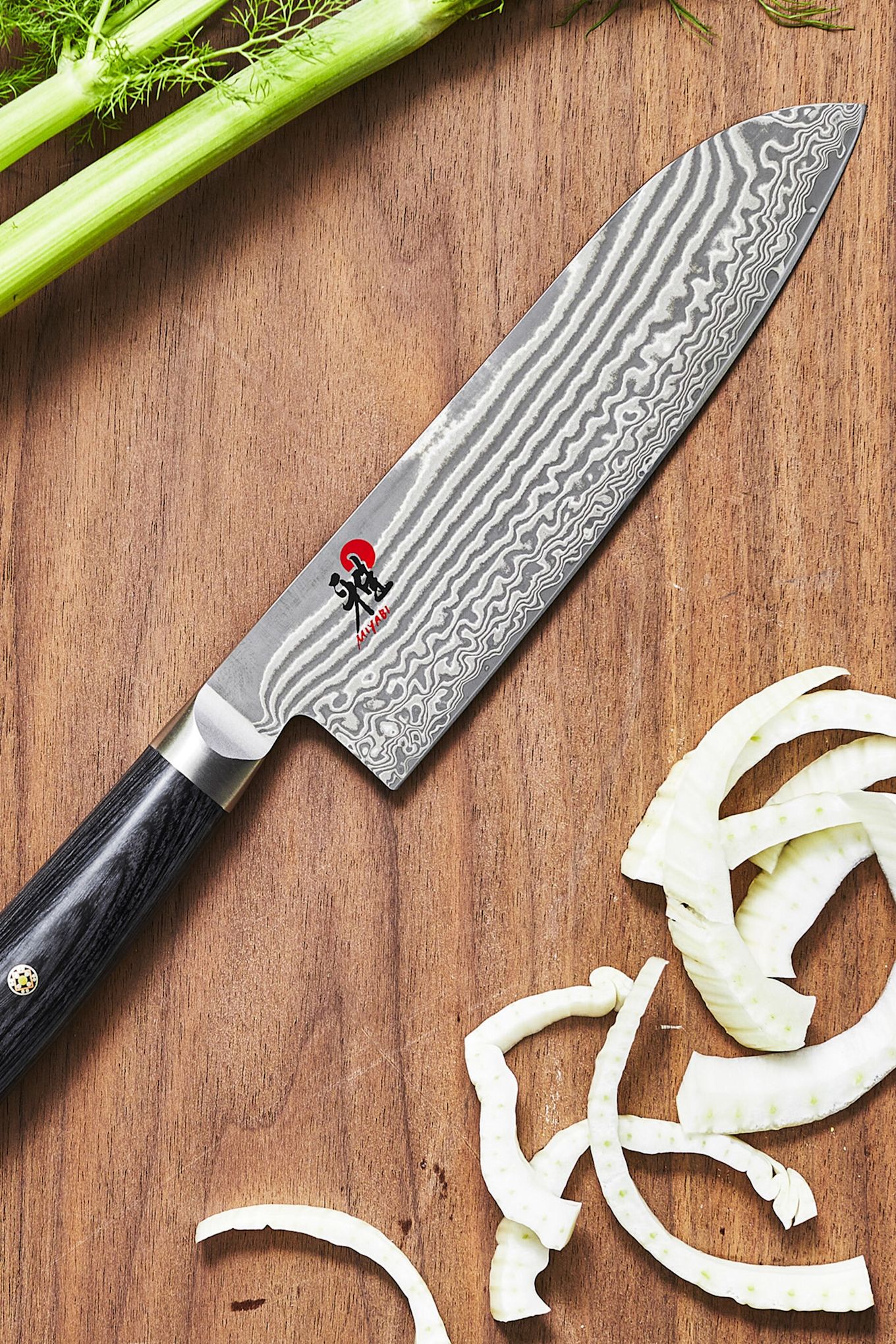 A close up of the Japanese Santuko knife from Miyabi on a wooden chopping board with chopped vegetables. 