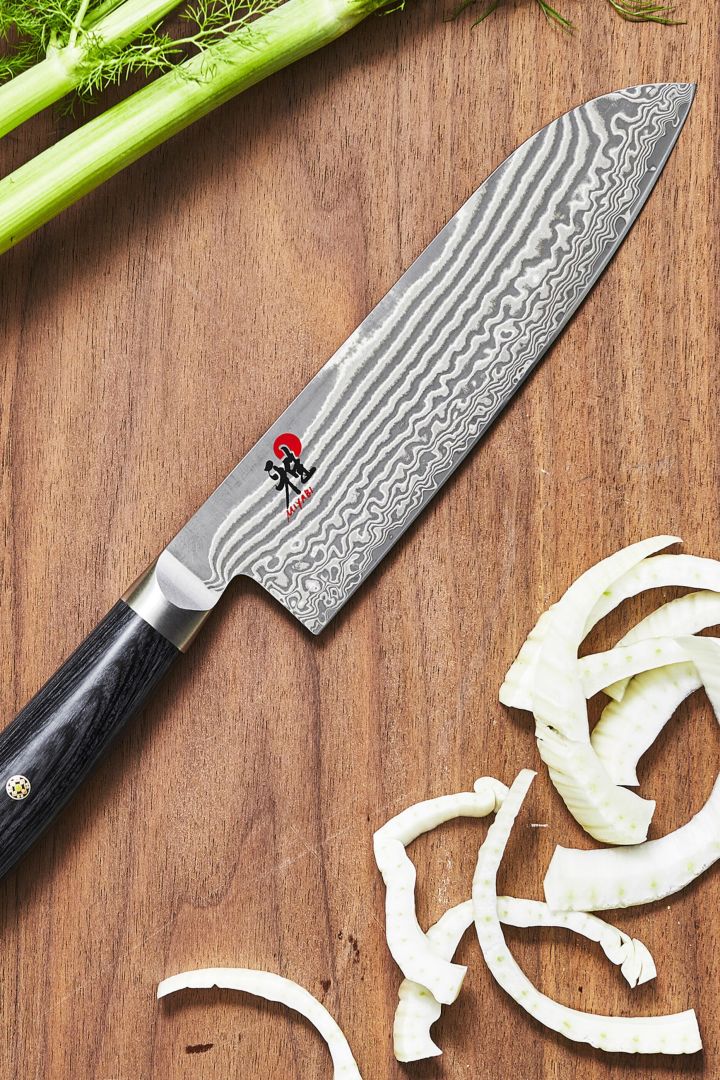 A close up of the Japanese Santuko knife from Miyabi on a wooden chopping board with chopped vegetables. 