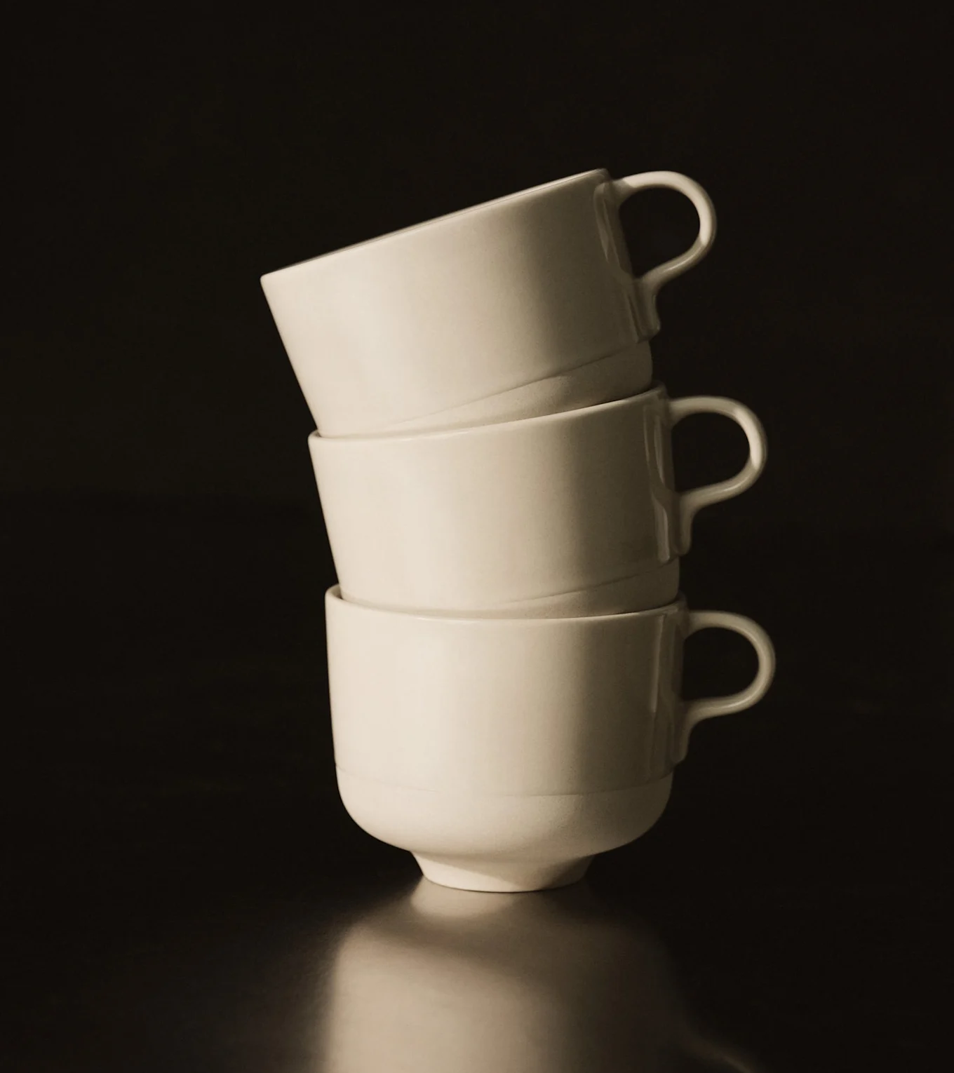 Three white ceramic cups stacked vertically on a dark, reflective surface.