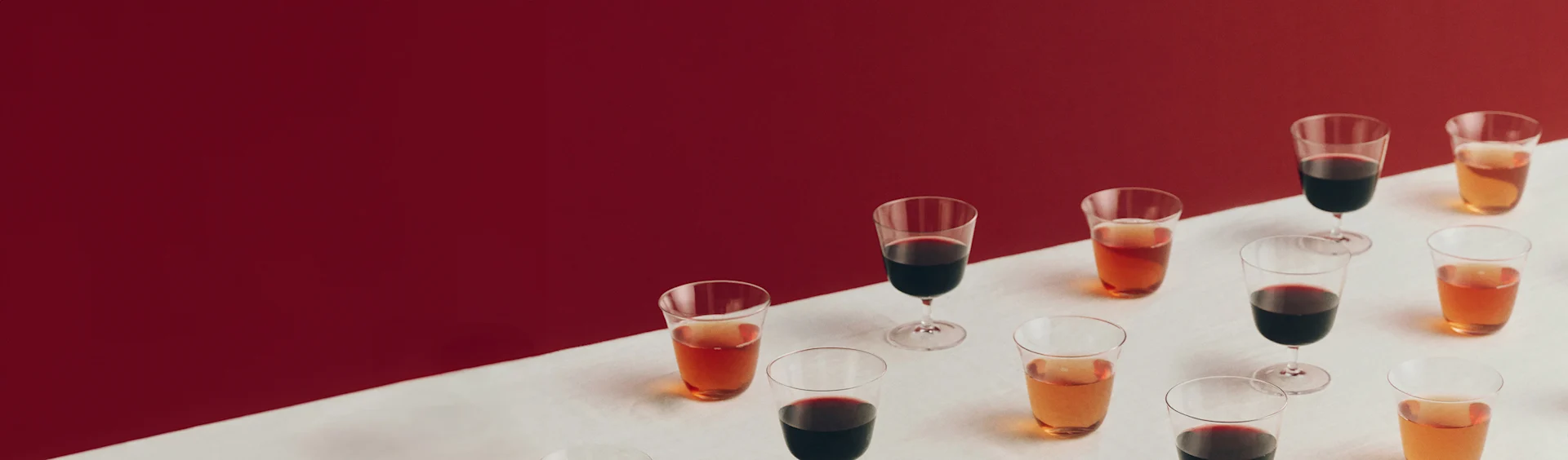 Various glasses with red and amber drinks on a white surface with a red background.
