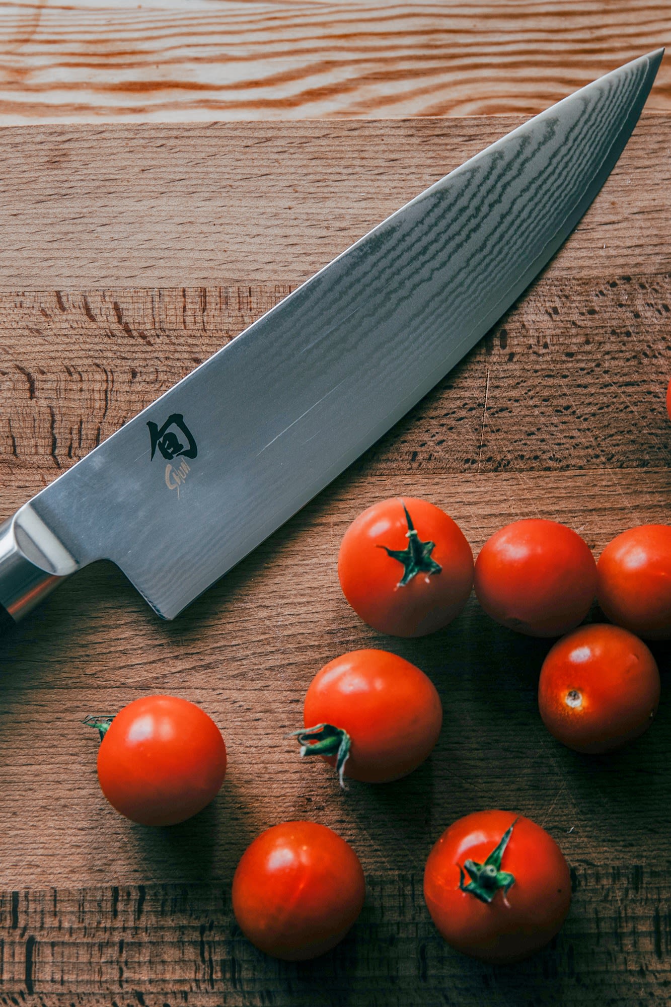 A close up of a Kai Shun Gyuto knife on a wooden chopping board with tomatoes.